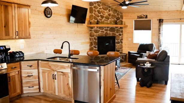 A cozy cabin interior with a kitchen island, wooden cabinets, a stone fireplace, and a comfortable seating area. - Entire Cabin in Linn, MO with all the extras (Linn)