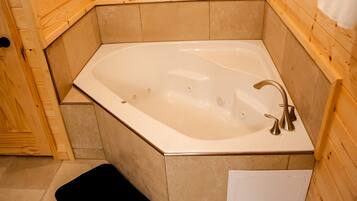 A corner bathtub with a wooden surround, a black bath mat, and a white towel on the wall.