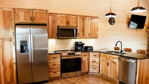 A modern kitchen with wooden cabinets, stainless steel appliances, a coffee station, and pendant lighting. - Entire Cabin in Linn, MO with all the extras (Linn)