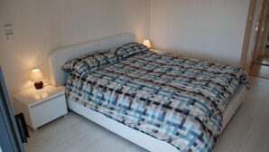 A neatly made bed with a checkered bedspread, a bedside table with a lamp, and a nightstand. - Beautiful Apartment in the heart of Palm Beach, Cannes (Cannes)