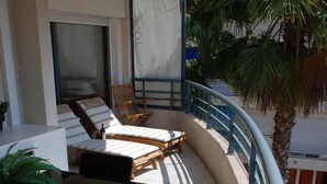 A sunlit outdoor balcony with a curved railing, a seating area with a table and chairs, and a potted plant. - Beautiful Apartment in the heart of Palm Beach, Cannes (Cannes)