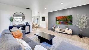 Ein modernes Wohnzimmer mit einem grauen Sofa, einem schwarzen Couchtisch und einem Baumgemälde an der Wand.