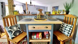 A cozy dining area with a wooden table, two chairs, a small cabinet with kitchen items, and a hanging light fixture. - Cabin in New Forest With Private Woodland (Romsey)