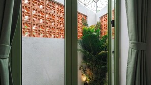 Vista a través de una ventana con una cortina verde, mostrando una pared blanca y un panel de madera decorativo con un diseño geométrico.