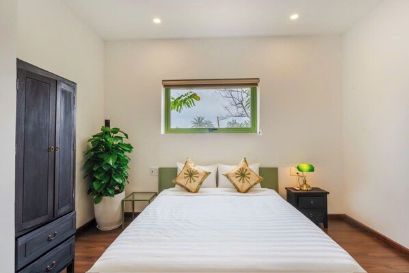 A bedroom with a bed, a nightstand, a lamp, a potted plant, and a wardrobe.