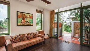 Una habitación con sofá, ventilador de techo, ventana grande y puerta que da al exterior.