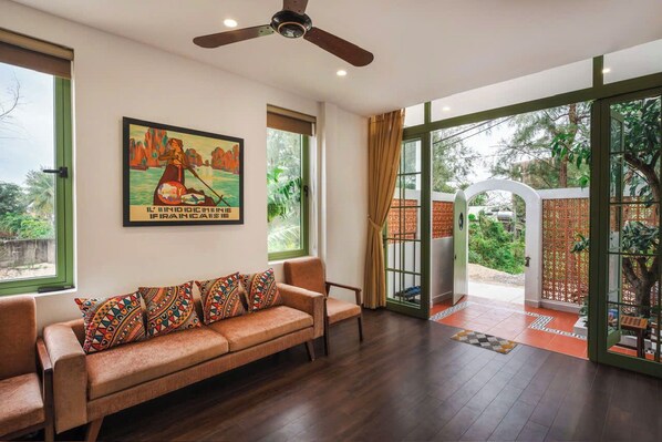 A room with a sofa, a ceiling fan, a large window, and a door leading outside.