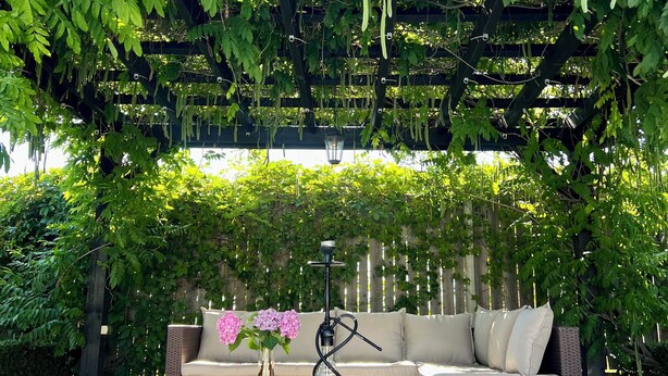 Un espace extérieur aménagé, abrité et doté de mobilier en osier, d’un narguilé et de plantes vertes suspendues.