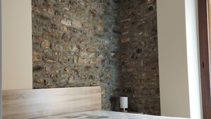 Ein Schlafzimmer mit einer Steinsäule, einem Bett mit Holz-Kopfstück und einem Nachttisch mit Lampe.