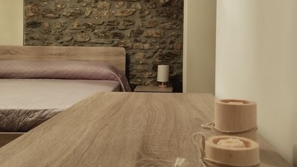Ein Zimmer mit Steinwand, einem Holztisch mit Kerzen und einem Bett mit rosa Decke.