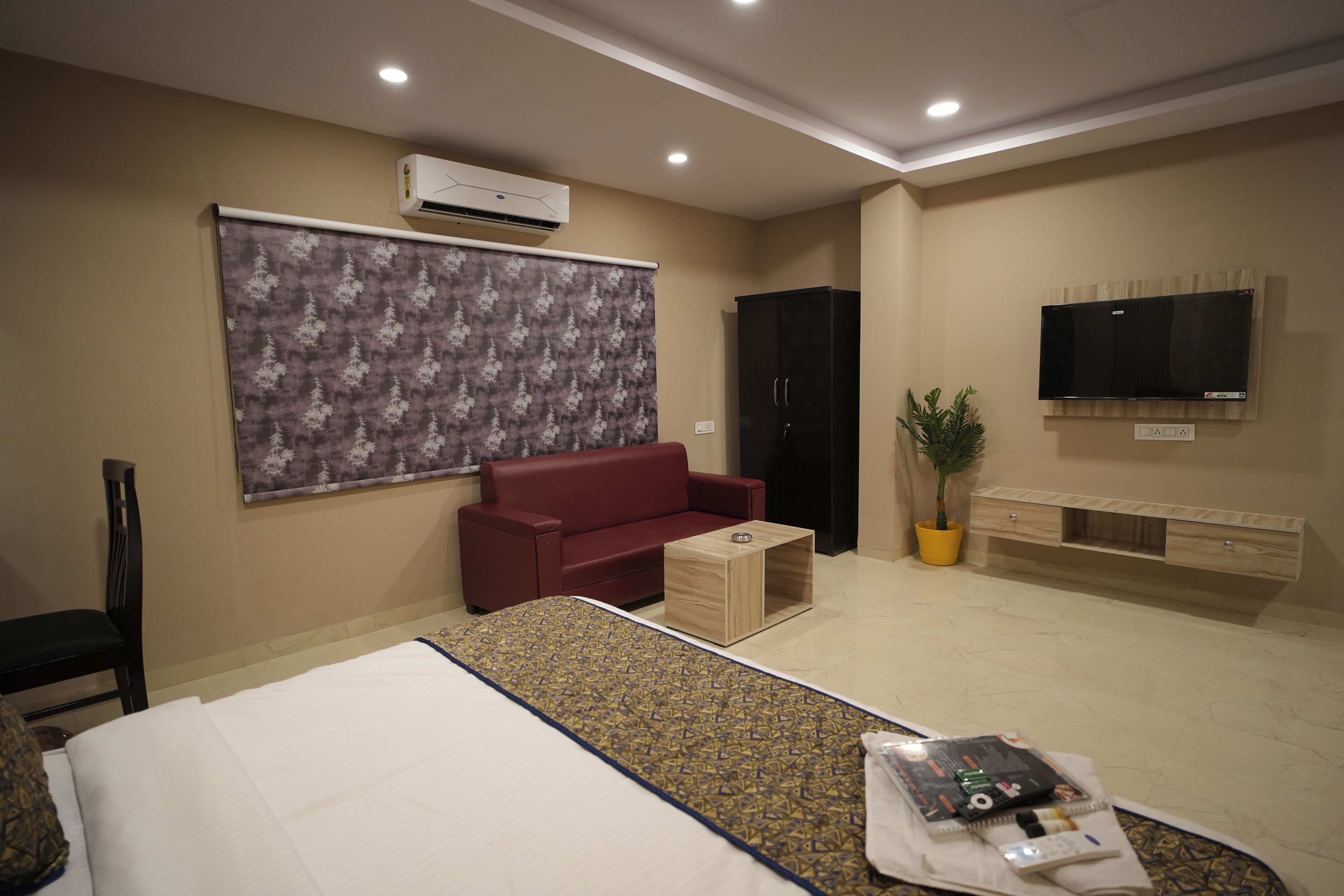 Ein Hotelzimmer mit einem Bett, einem roten Sofa, einem kleinen Holzhochentisch, einem an der Wand montierten Fernseher und einer Klimaanlage.