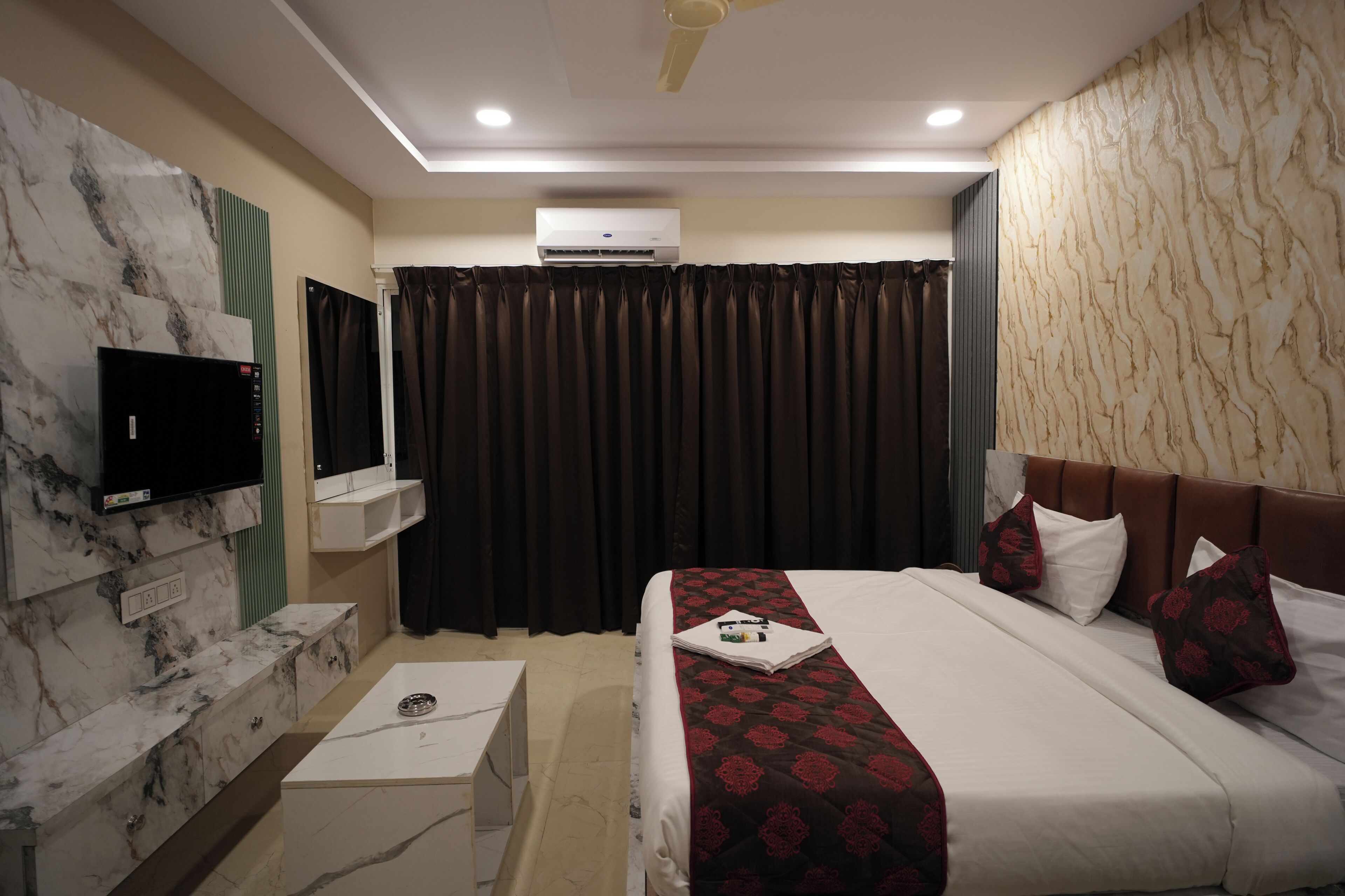A hotel room with a bed, a TV, an air conditioner, and a marble wall.