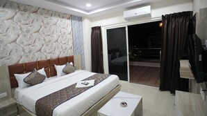 A modern hotel room with a large bed, a nightstand, a small table, a ceiling fan, and a sliding glass door leading to a balcony.