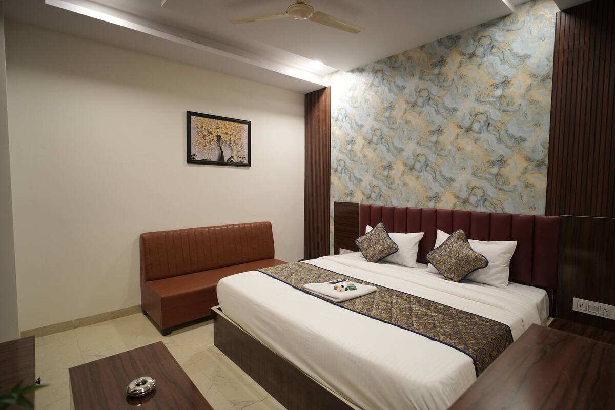 A hotel room with a bed, a sofa, a wooden coffee table, and a ceiling fan.