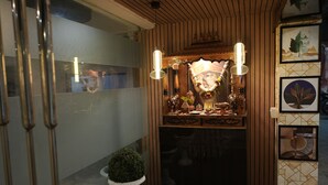 A reception area with a wooden ceiling, a glass partition, and a reception desk with a decorative backdrop. There are two potted plants and a small round table in front of the desk.