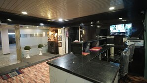 A modern hotel lobby with a marble reception desk, a large flat-screen TV, and a seating area with a patterned rug.