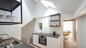 A modern kitchen with a central island, a built-in oven, and a black countertop. There is a window above the sink and a skylight in the ceiling. - NEXT TO CAFÉ DE FLORE & LES DEUX MAGOTS -3 BEDROOM PARISIAN CHARM AT RUE GOZLIN (Paris)