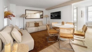 A modern living room with a sofa, a dining table with chairs, a flat-screen TV, and a large mirror. - NEXT TO CAFÉ DE FLORE & LES DEUX MAGOTS -3 BEDROOM PARISIAN CHARM AT RUE GOZLIN (Paris)
