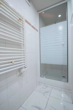 A bathroom with white tiled walls, a glass shower enclosure, and a white radiator. - Cozy Studio - 2P - Buttes-chaumont (Paris)