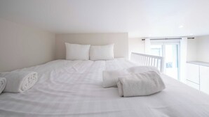 A spacious bedroom with a large bed, white bedding, and a balcony with a railing. - Cozy Studio - 2P - Buttes-chaumont (Paris)