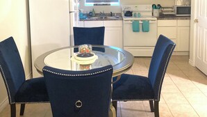 A compact kitchen with white cabinets, a dining table with chairs, and a window with sheer curtains.
