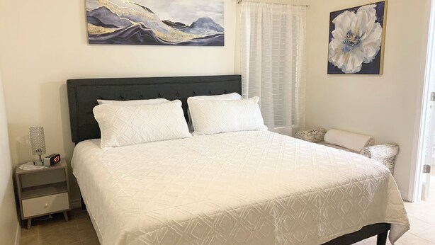 A neatly made bed with a quilted pattern, a bedside table with a lamp, and two wall-mounted paintings.