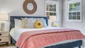 Une chambre à coucher avec un lit, des tables de chevet, un miroir fixé au mur et des fenêtres.