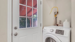 Une buanderie avec un lave-linge blanc, une fenêtre surmontée d’un toit rouge et un chauffe-eau fixé au mur.