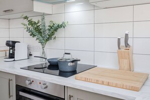 A modern kitchen with a built-in stove, a coffee maker, a pot, a cutting board, and a knife block.