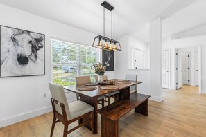 Uma sala de jantar com mesa de madeira, cadeiras, um banco e uma luminária pendente.