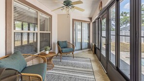 A covered porch with a ceiling fan, wicker furniture, and large windows.