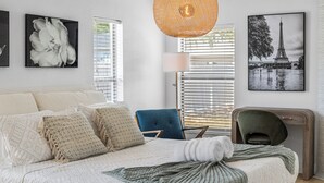 A bedroom with a bed, a chair, a desk, and a hanging light fixture.