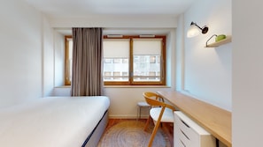 A hotel room with a bed, a desk, a chair, a window with curtains, and a view of buildings outside. - Comfort Studio in a Premium Residence- Sport/rooftops (Paris)