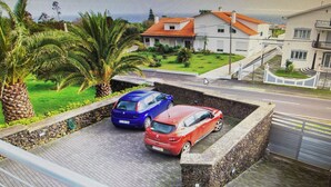 A residential area with two cars parked in a driveway, a house with a red roof, and a palm tree. - PORTO MARTINS RELAX APARTMENT - AL (Porto Martins)