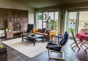 Een woonkamer met een open haard, een bank, een salontafel en een eethoek met een tafel en stoelen.