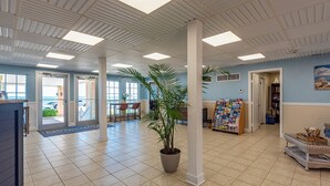 A spacious lobby with a tiled floor, a reception desk, a potted plant, and a bookshelf. - Galveston condo on Seawall near beach, gulf view, pools, WiFi, fitness room. (Galveston)
