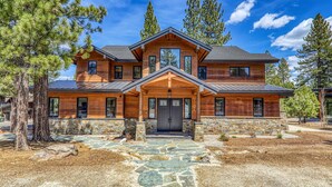 A two-story log cabin with a stone foundation, large windows, and a prominent front porch. - Aloha Mountain Haus | Luxury Golf Retreat | Club Access | Billiards (Truckee)