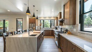 A modern kitchen with a central island, wooden cabinets, and pendant lighting. - Aloha Mountain Haus | Luxury Golf Retreat | Club Access | Billiards (Truckee)