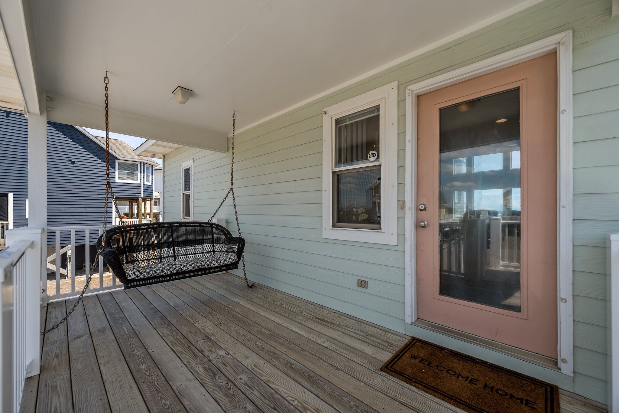 A porch with a swing chair, a door with a window, and a welcome mat.