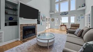Een ruime woonkamer met een open haard, een grote flatscreen televisie en een ronde glazen salontafel.