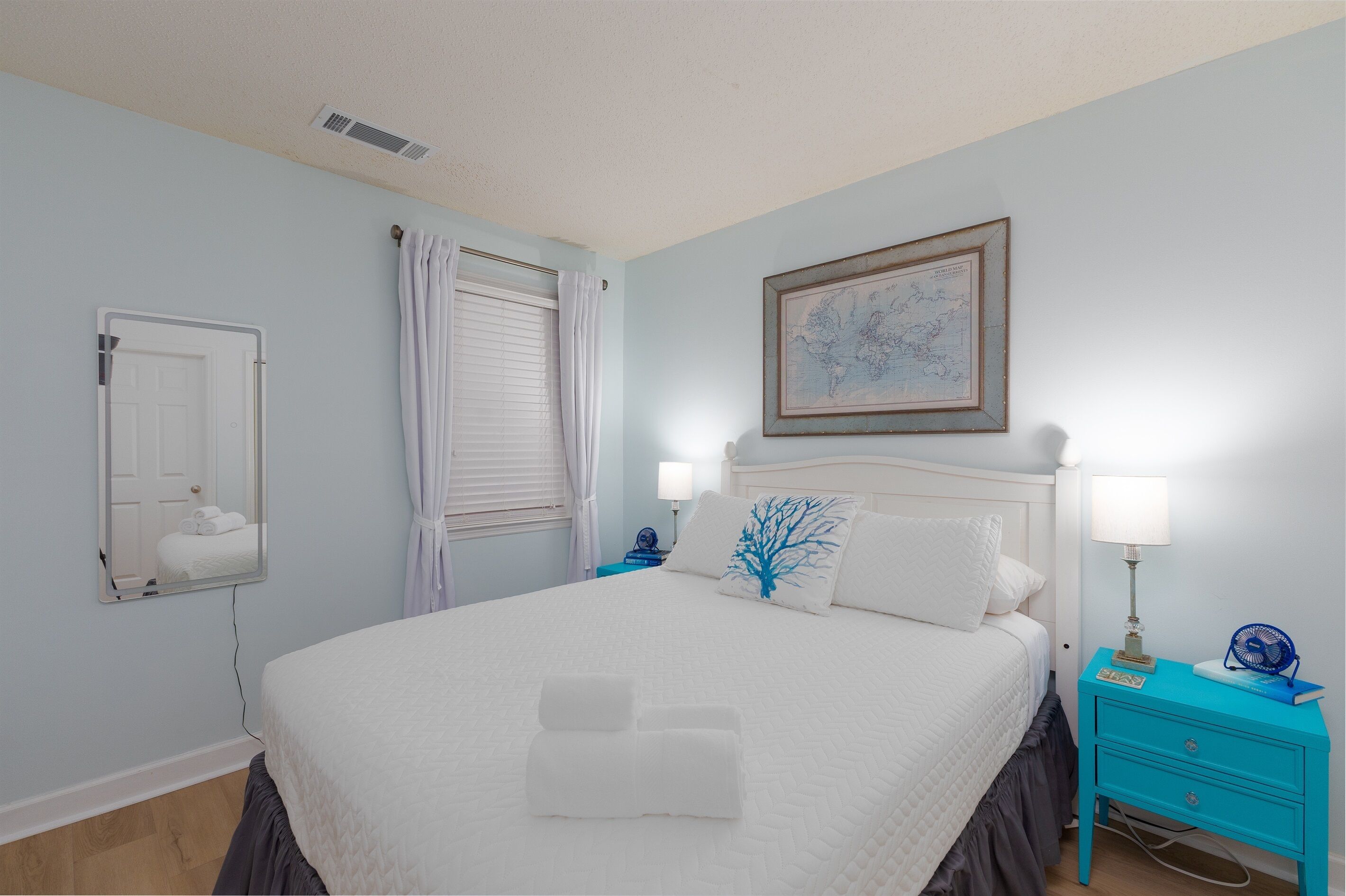 A neatly made bed with white linens, a bedside table with a lamp, and a wall-mounted map.