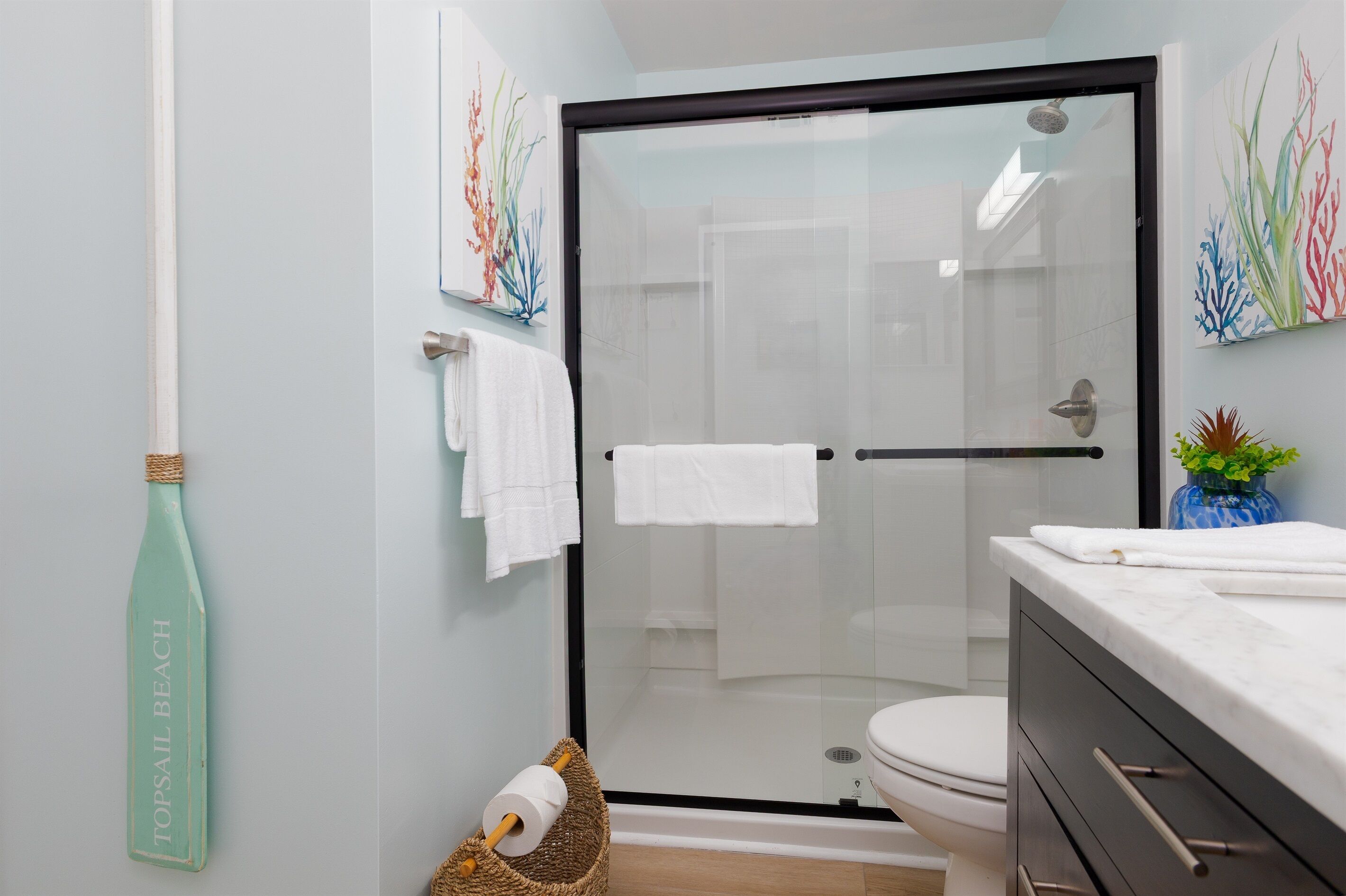 A modern bathroom with a glass shower enclosure, a toilet, and a sink with a marble countertop.