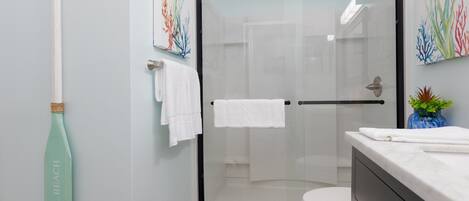 A modern bathroom with a glass shower enclosure, a toilet, and a sink with a marble countertop.