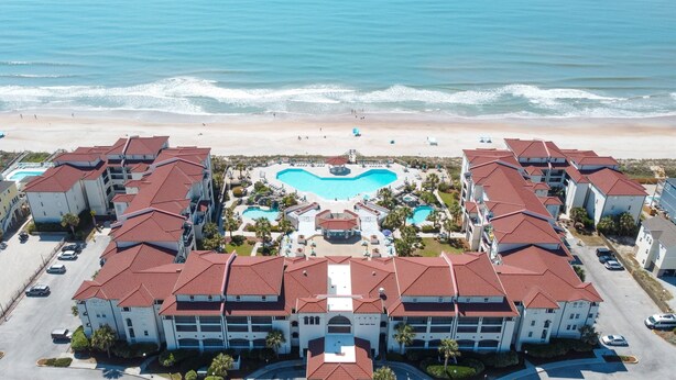 Ein Resort mit einem zentralen Schwimmbad, Blick auf den Strand und mehreren Gebäuden mit roten Ziegeldächern.