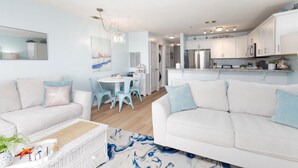 Ein modernes Wohnzimmer mit zwei weißen Sofas, einem Essbereich mit blauen Stühlen und einer Küche mit weißen Schränken.