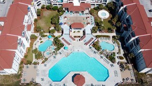 Eine Vogelperspektive zeigt ein Hotel mit mehreren Schwimmbecken, einem Innenhof und umgebenden Gebäuden mit roten Dächern.