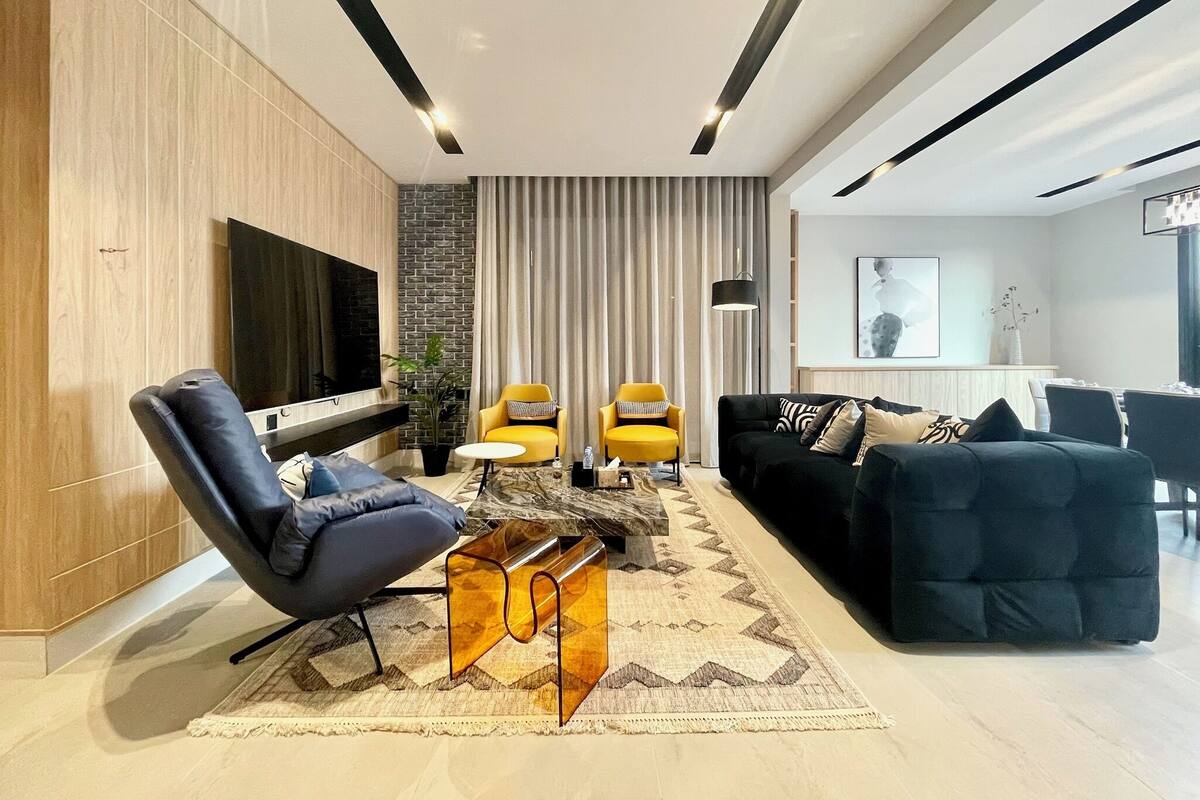 A modern living room with a TV, two yellow armchairs, a black sofa, and a coffee table.