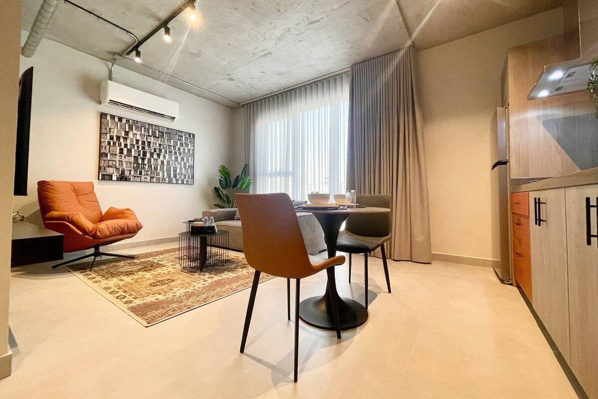 A modern living room with a sofa, a dining table with chairs, a coffee table, and a large plant.