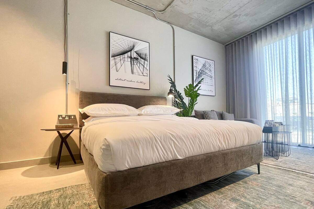 A modern bedroom with a large bed, a bedside table, a plant, and two abstract art pieces on the wall.