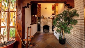 A cozy interior with a fireplace, wooden beams, and potted plants.